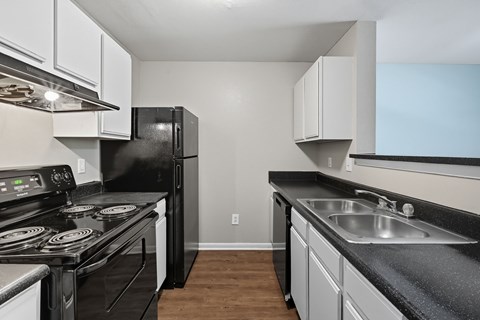 A black refrigerator sits in a kitchen with white cabinets.