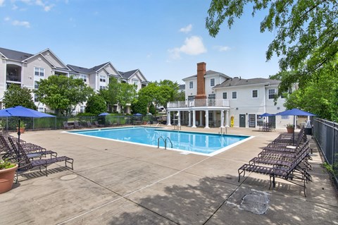 A swimming pool surrounded by lounge chairs and umbrellas in a residential area.