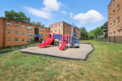 A playground with a red slide and a blue slide in the middle of a grassy area at Huntwood Courts Apartments, Washington DC