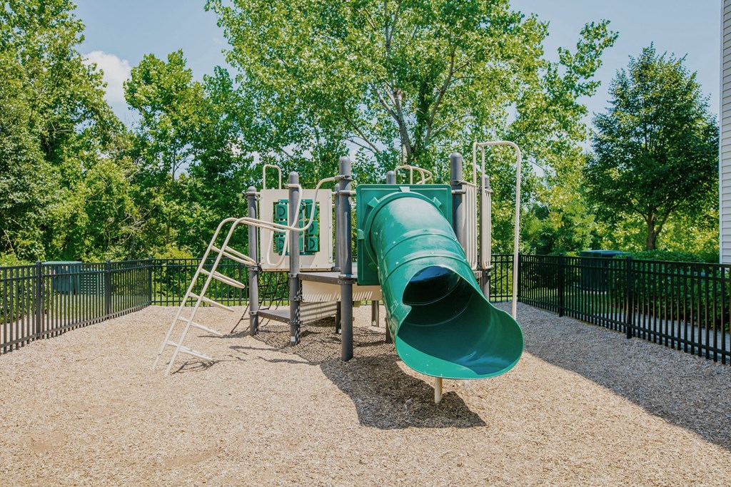 a large green slide in a park with trees in the background