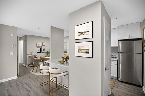 A kitchen with a refrigerator, a dining table with chairs, and pictures on the wall.