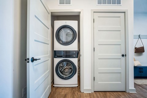 A white door with a black handle is open to reveal a washing machine and dryer.