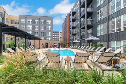 A pool surrounded by chairs and umbrellas in front of apartment buildings.