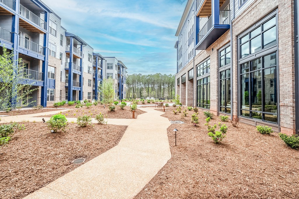 a walkway between two apartment buildings with trees in the background at Preston Ridge, North Carolina
