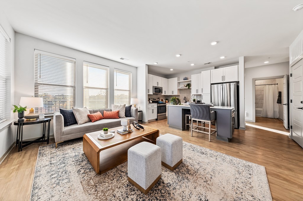 A modern living room with a grey sofa, a wooden coffee table, and a kitchen area in the background