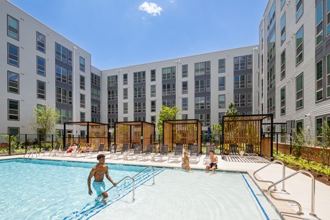 People are enjoying the pool at a resort with apartment buildings in the background.