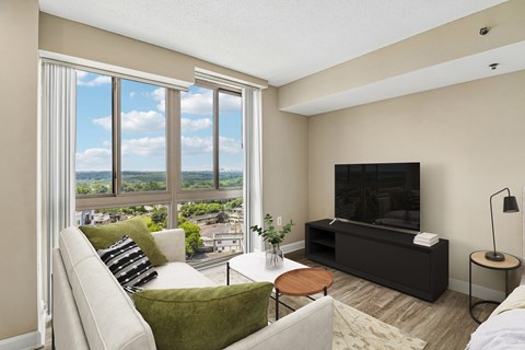 A living room with a couch, a chair, a coffee table, a television, and a window with a view of the city.