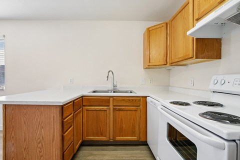 A kitchen with a white stove top oven and wooden cabinets.
