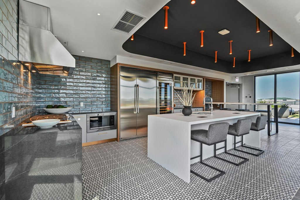 A modern kitchen with a long white island and grey chairs.