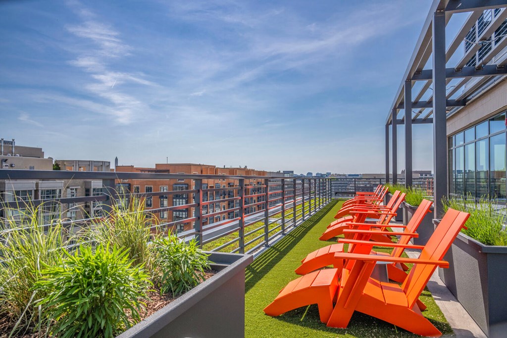 A rooftop patio with orange chairs and a metal railing.