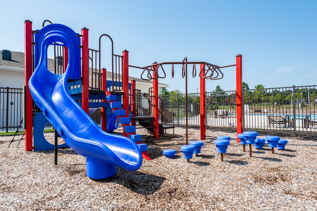 a playground with a blue slide and chairs on the ground