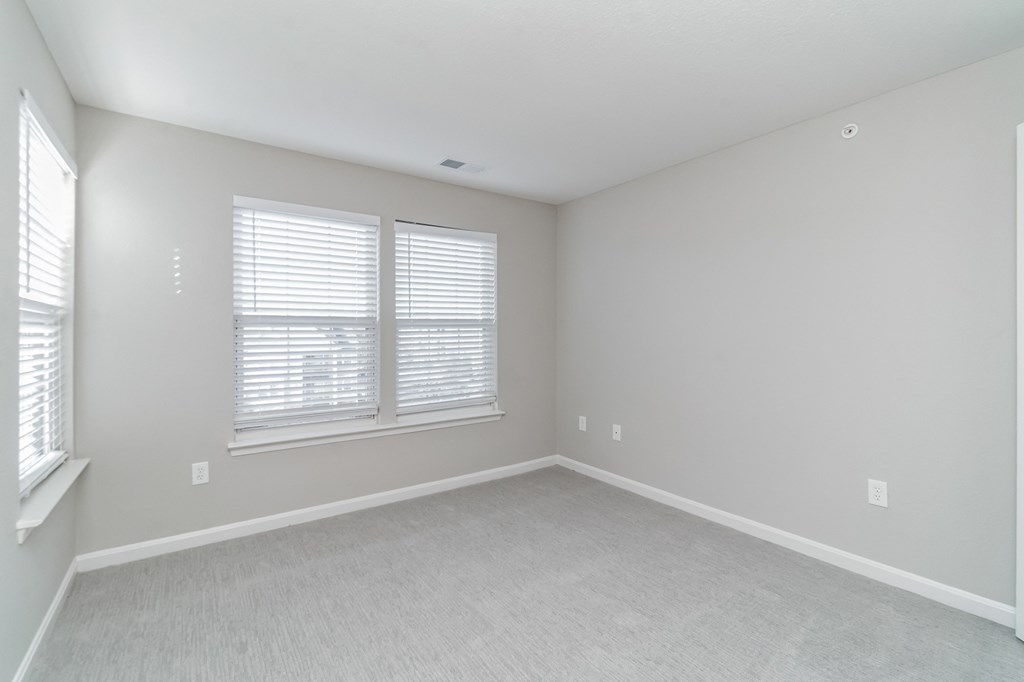 an empty bedroom with two windows and white carpeting at The Fields at Lorton Station, Lorton, VA