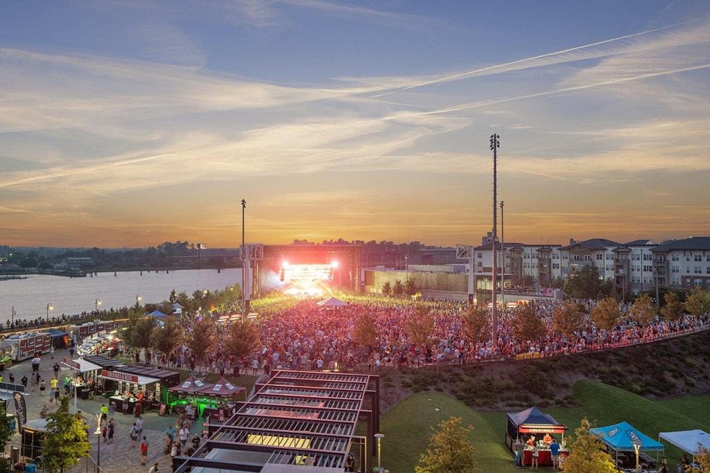 a crowd of people sitting on top of a grass covered field at Metropolitan at the Riverwalk, Wilmington, NC