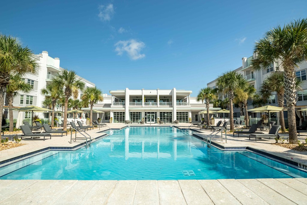 a resort style swimming pool with chaise lounge chairs and palm trees in front of a white at Delamarre at Celebration, Florida