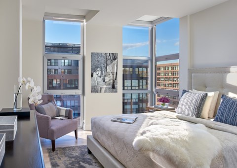 A bedroom with a large bed and a chair by a window.