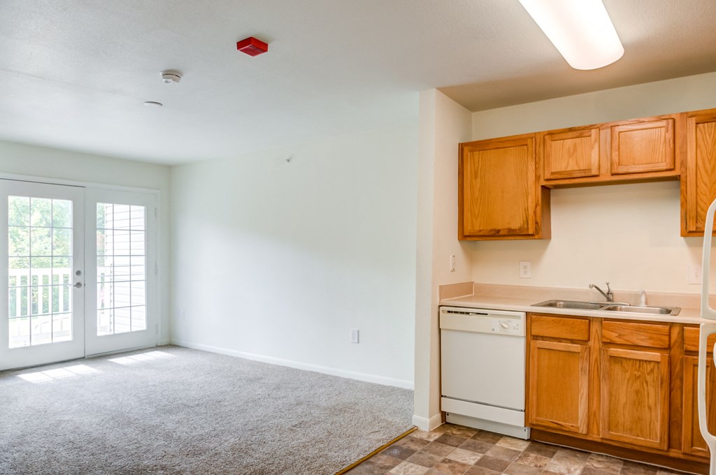 a kitchen and living room with white walls and brown cabinets