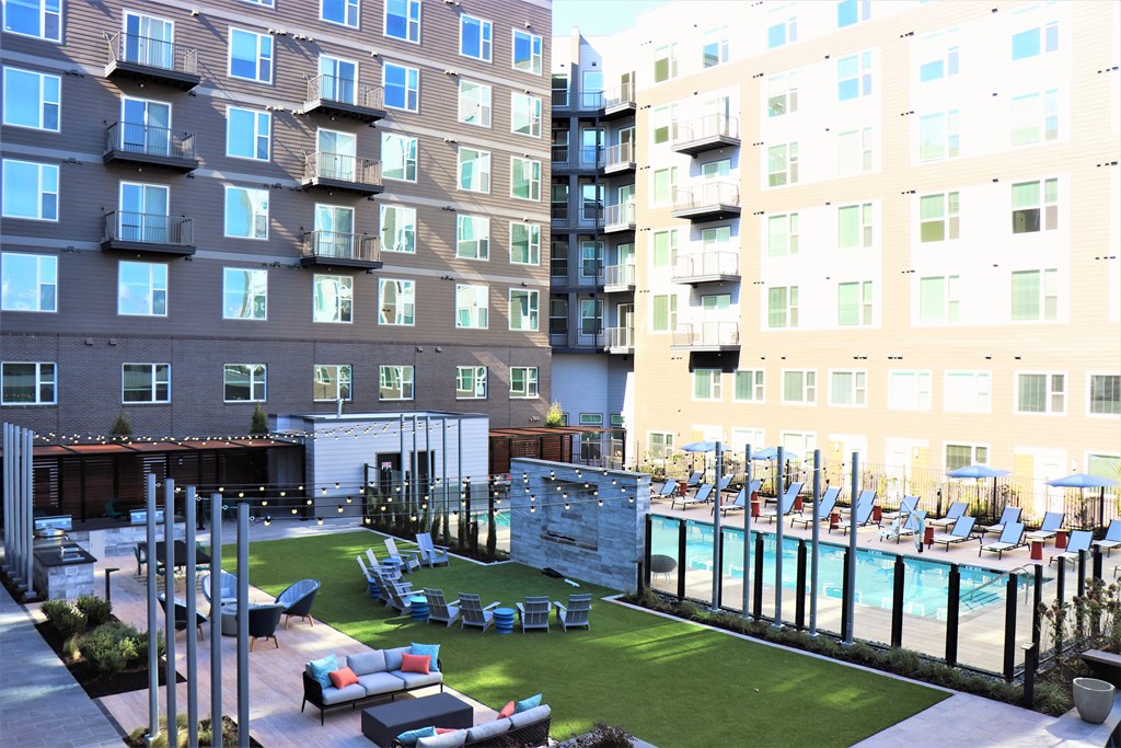 an outdoor lounge area with lounge chairs and a pool next to an apartment building at Vyne One Loudoun, Virginia