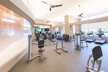 a gym with weights and cardio equipment in a large room with windows at The Acadia at Metropolitan Park Apartments in Arlington, VA 22202