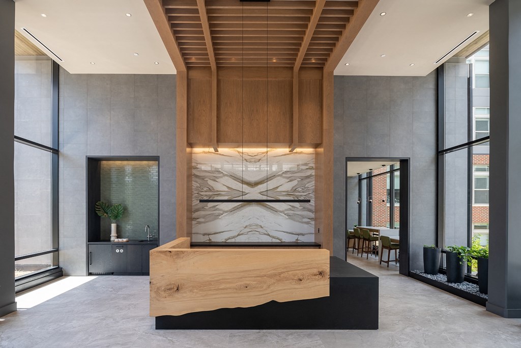a large wooden front desk with a marble fireplace in the middle of a lobby at Brentford at The Mile, Tysons, Virginia