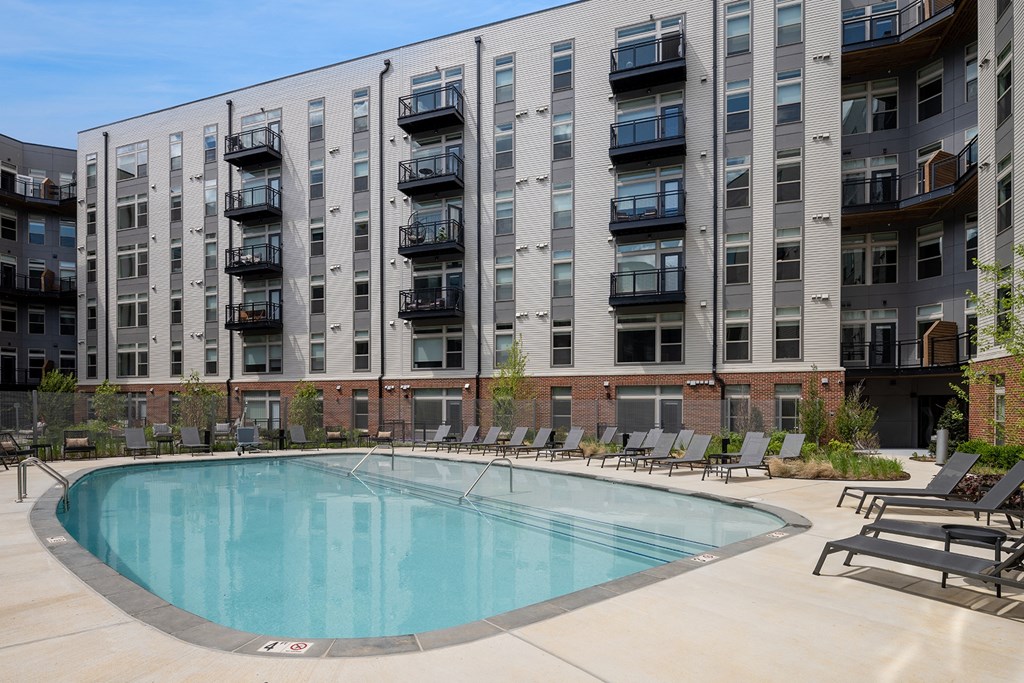 a swimming pool with chaise lounge chairs and an apartment building in the background at Brentford at The Mile, Tysons
