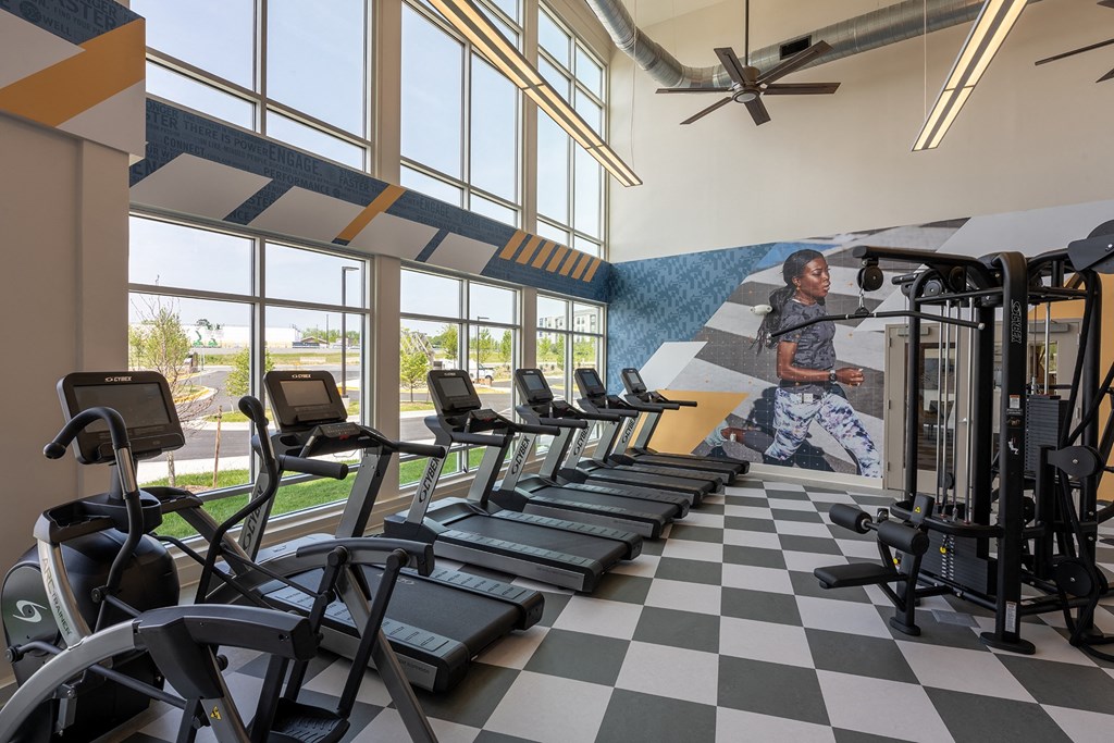a woman runs on a treadmill in front of a wall of windows with a mural of a  at Woodmore Grand, Bowie, 20721