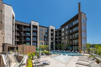 a pool with lounge chairs in front of an apartment building