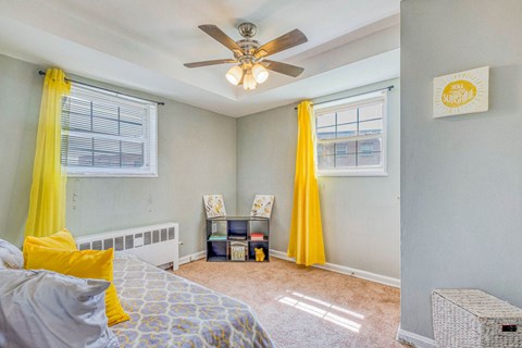 A bedroom with a bed, a ceiling fan, and yellow curtains at Huntwood Courts Apartments, Washington, DC, 20019