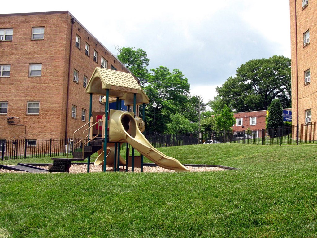 A playground with a yellow slide in front of a brick building. A playground with a yellow slide in front of a brick building at Huntwood Courts Apartments, Washington, Washington DC