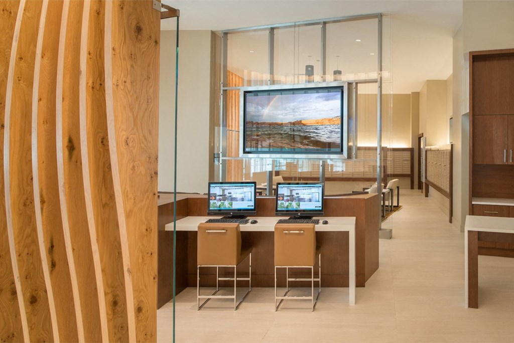 a desk with two laptops and two chairs in front of a large screen at The Acadia at Metropolitan Park, Arlington, 22202
