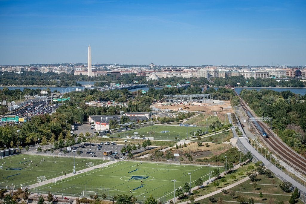 an aerial view of a football field in a city with a river in the background at The Acadia at Metropolitan Park, Arlington, Virginia