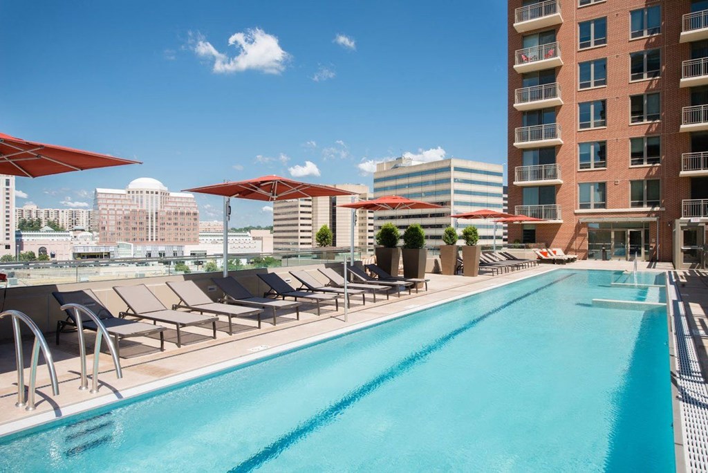 a swimming pool with lounge chairs and umbrellas next to a tall building at The Acadia at Metropolitan Park, Arlington, VA