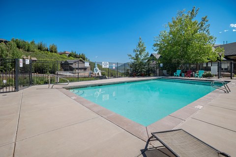 A large outdoor swimming pool surrounded by a fence and lounge chairs.