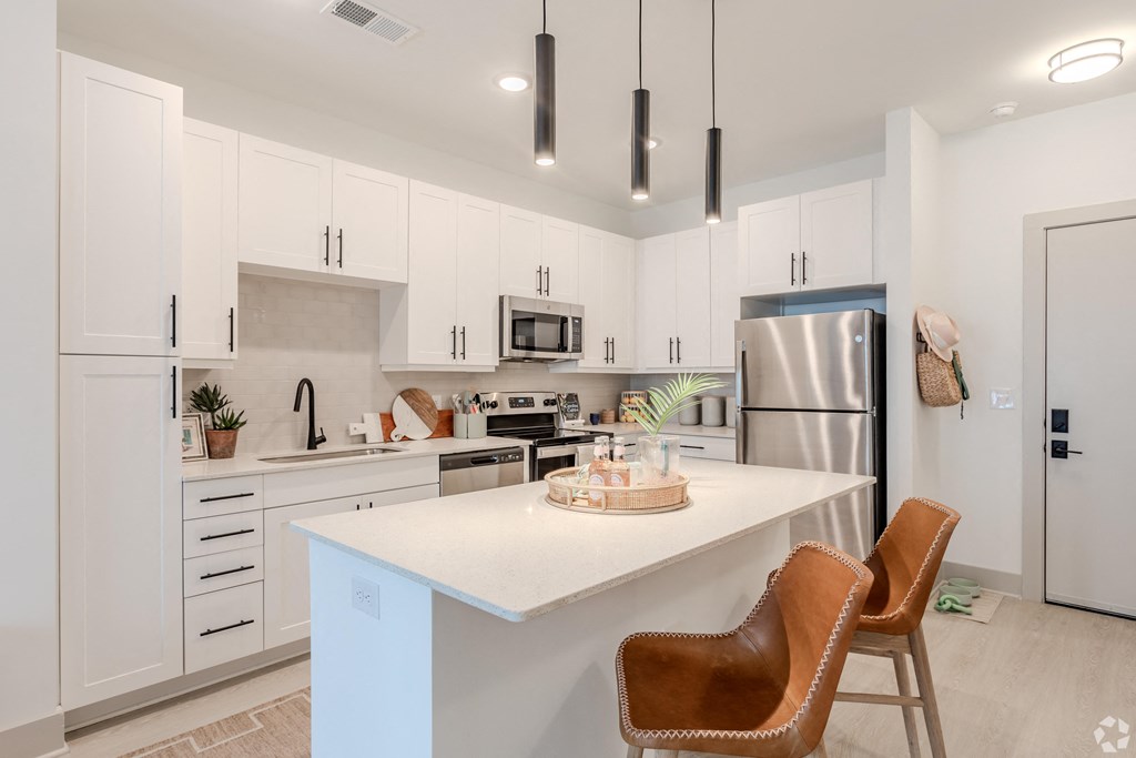 an open kitchen with white cabinets and a white island with two chairs at Metropolitan at the Riverwalk, Wilmington North Carolina