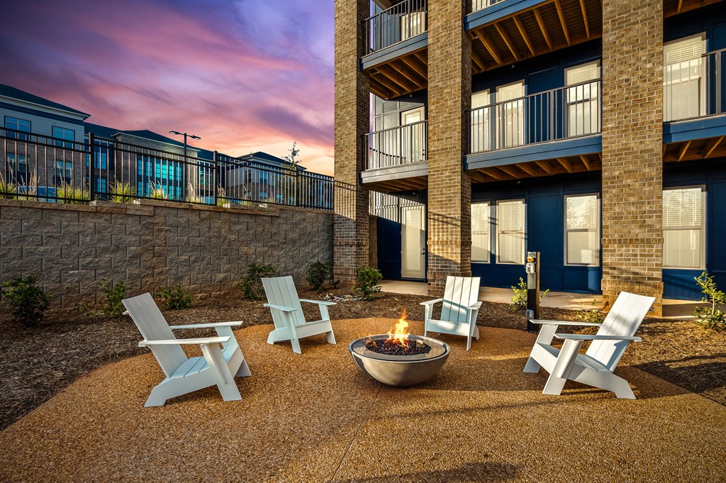 A fire pit sits in the middle of a gravel patio surrounded by four chairs