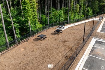 A black fence surrounds a dirt field with a picnic table and a trash can.