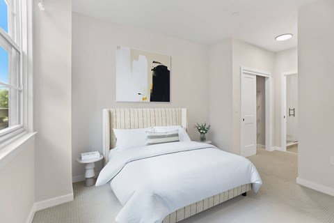 A white bedroom with a large bed and a small plant on the side table.