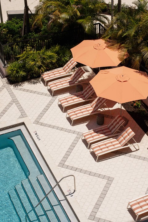 A pool with a striped sun lounger and umbrella next to it.