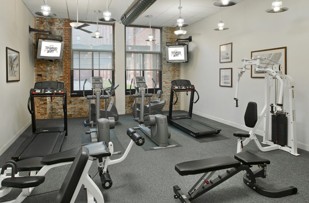 a gym with weights and exercise equipment in a room with windows a gym with weights and exercise equipment in a room with windows at Tindeco Wharf, Baltimore, MD