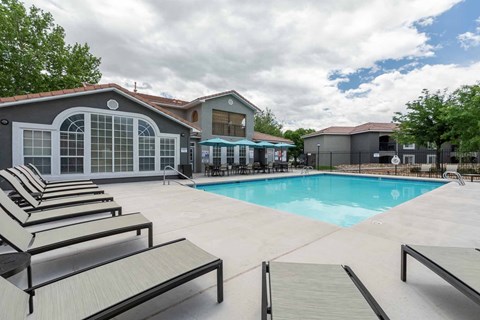 A pool area with sun loungers and a building in the background at West Park Apartments, Albuquerque