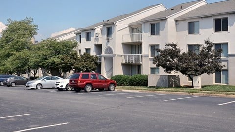 A red car is parked in a parking lot in front of apartment buildings.
