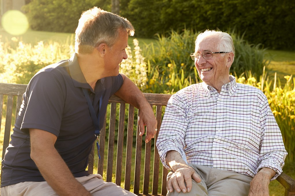 two men sitting on a park bench laughing