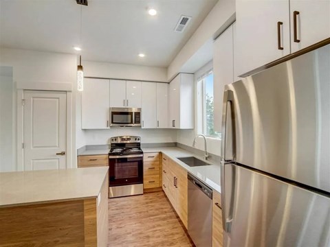 A modern kitchen with a stainless steel refrigerator and wooden flooring.