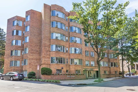 A large red brick building with many windows and a tree in front.