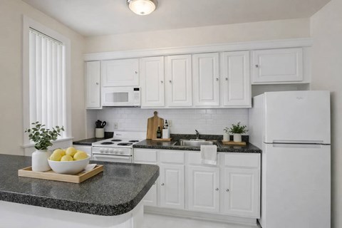A kitchen with white cabinets and appliances, a granite countertop, and a bowl of lemons on a cutting board.