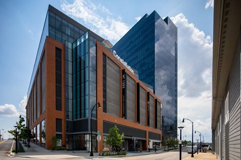 A modern building with a glass facade is situated next to a shorter brick building.