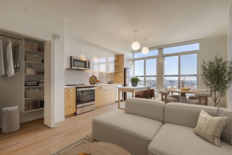 A modern living room with a grey couch and a kitchen area with wooden cabinets.