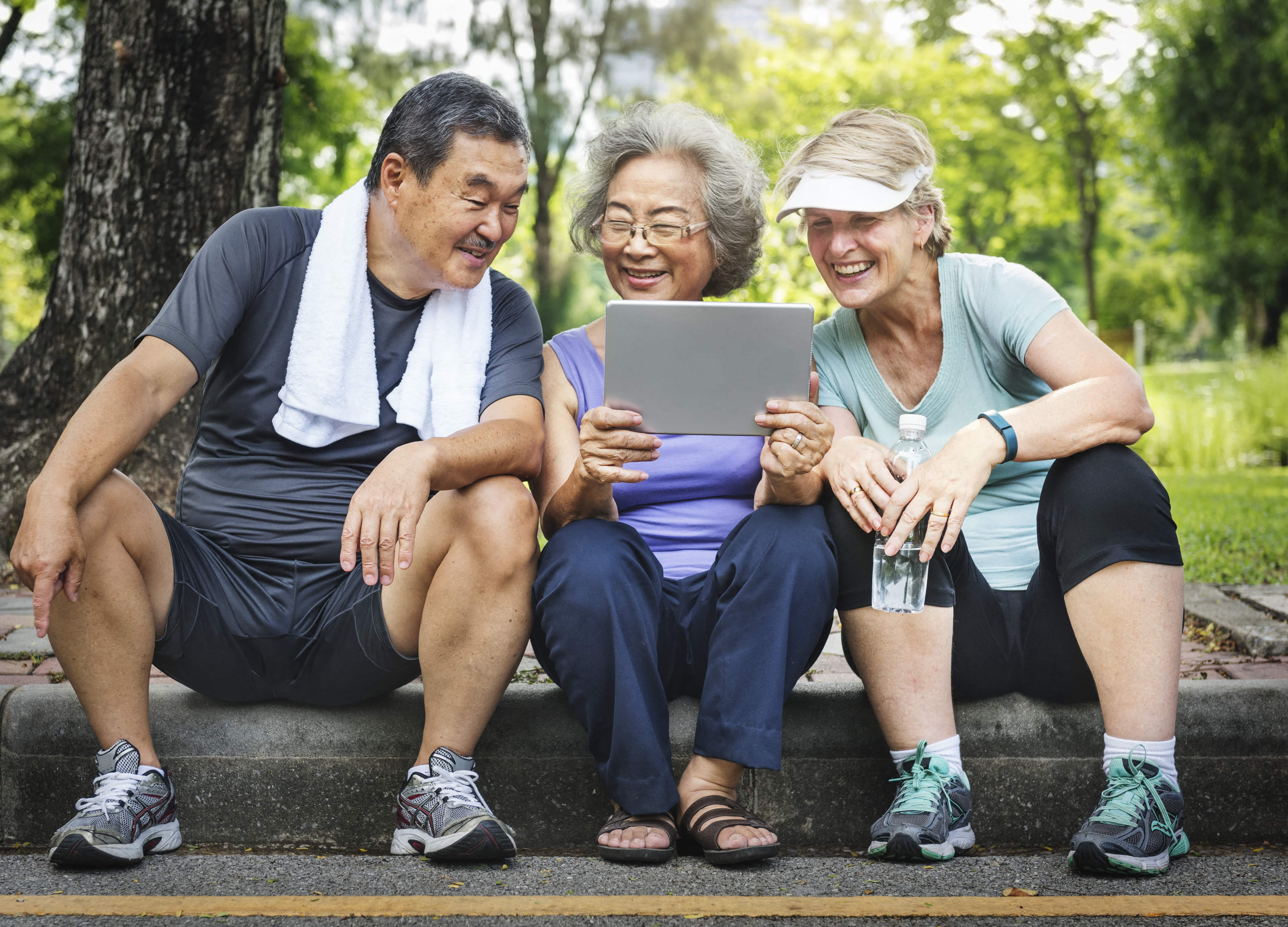 a man and two women sitting on a curb looking at a tablet