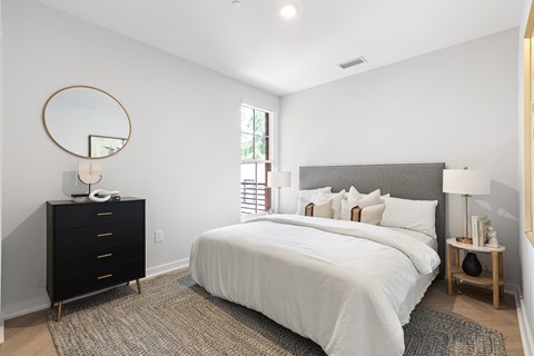 A bedroom with a large bed, a dresser, and a nightstand with a lamp.