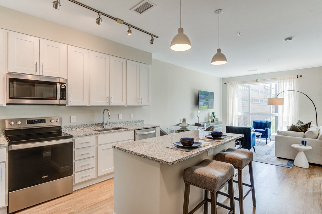 a kitchen with an island and stools in front of a living room with a couch and at Vesta Parkside, Washington, Washington