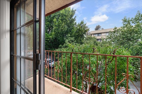 A balcony with a metal railing and a view of a green tree and a building.